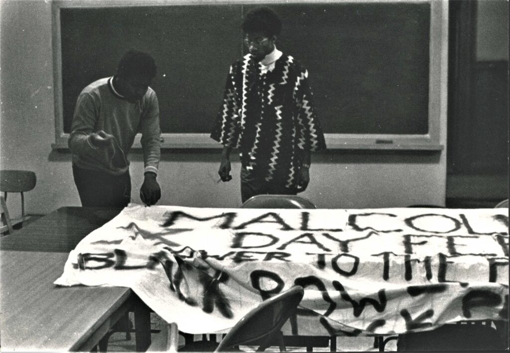 In this image, before the Fisk Hall Takeover took place, black students are shown spray-painting a banner that says: Malcolm X Day, Feb 21. Power to the Black People.